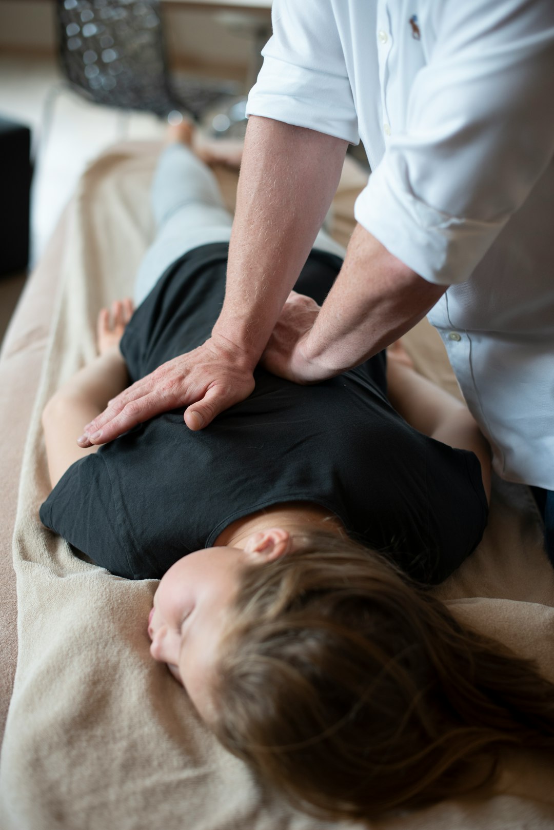 A woman sitting comfortably on an osteopathic table in a bright, minimalist clinic, looking relaxed and attentive during a consultation, warm natural light, sof