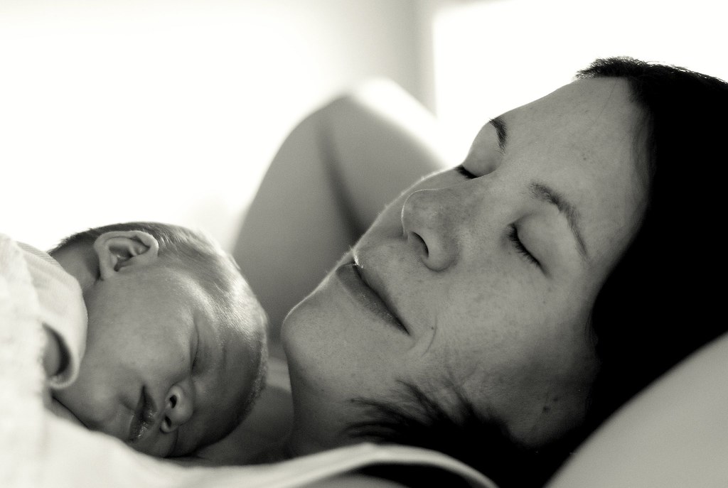 A calm newborn resting peacefully in a parent's arms near a bright window, soft natural light, warm and reassuring atmosphere, no clinical setting